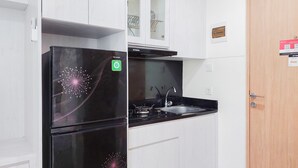 A compact kitchen with a black refrigerator, a stove, and a sink. There is a wooden door on the right and a white cabinet above the sink. - Serene And Homey Studio Apartment B Residence (Pagedangan)