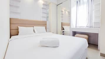 A neatly made bed with a white comforter and pillows, a bedside table, and a large mirror reflecting the room.