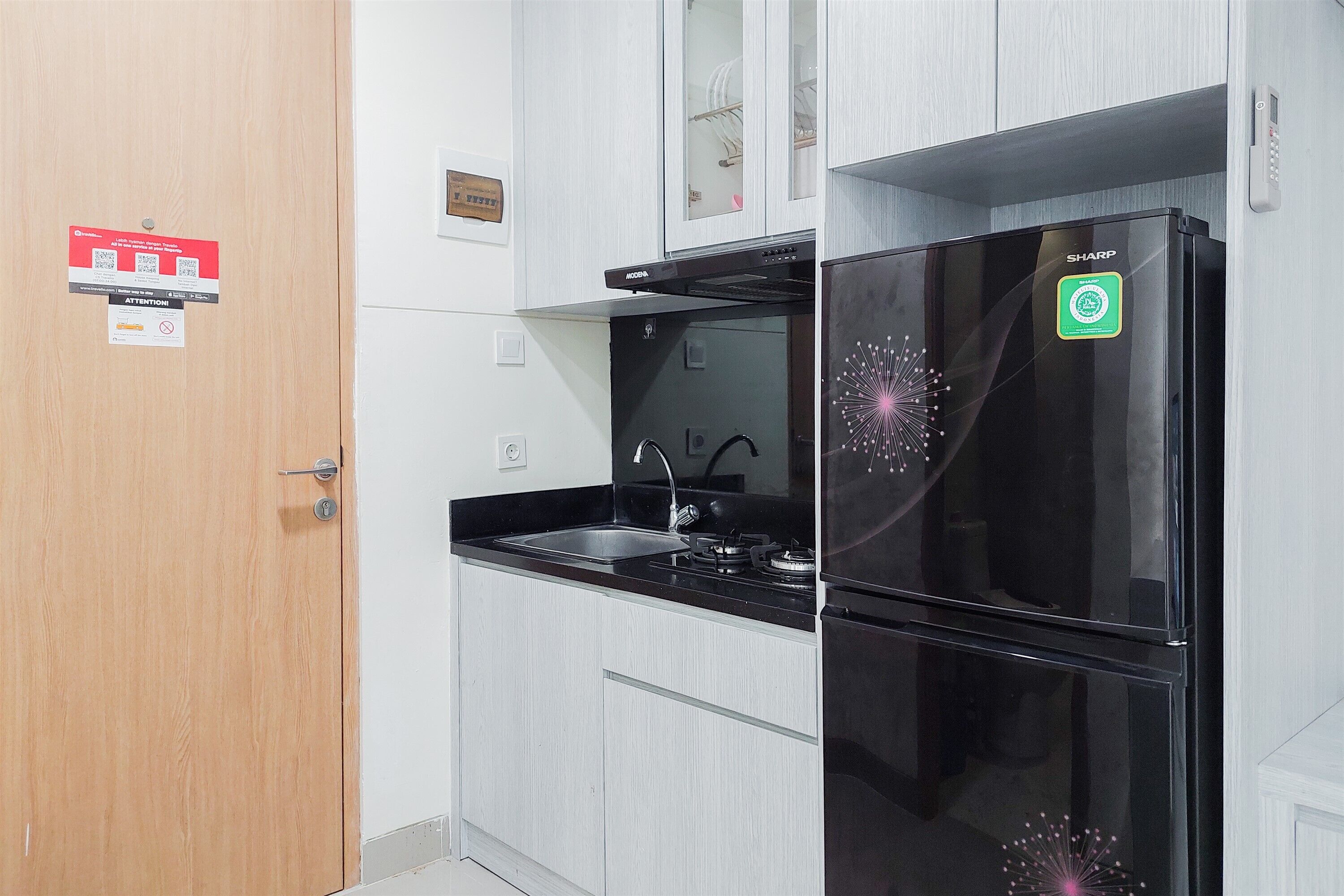 Uma cozinha moderna com geladeira preta, pia de aço inoxidável e porta de madeira.