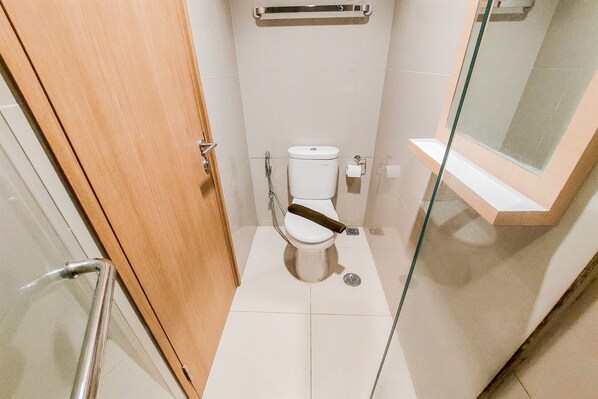 A small, modern bathroom with a toilet, a glass shower enclosure, and a wooden door.