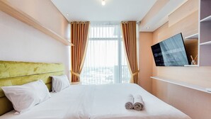 A hotel room with a large bed, a television on the wall, and a window with curtains.
