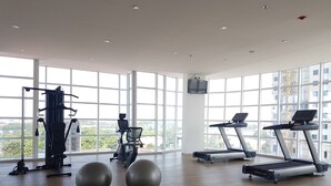 A spacious gym with large windows, exercise equipment, and a view of the city.
