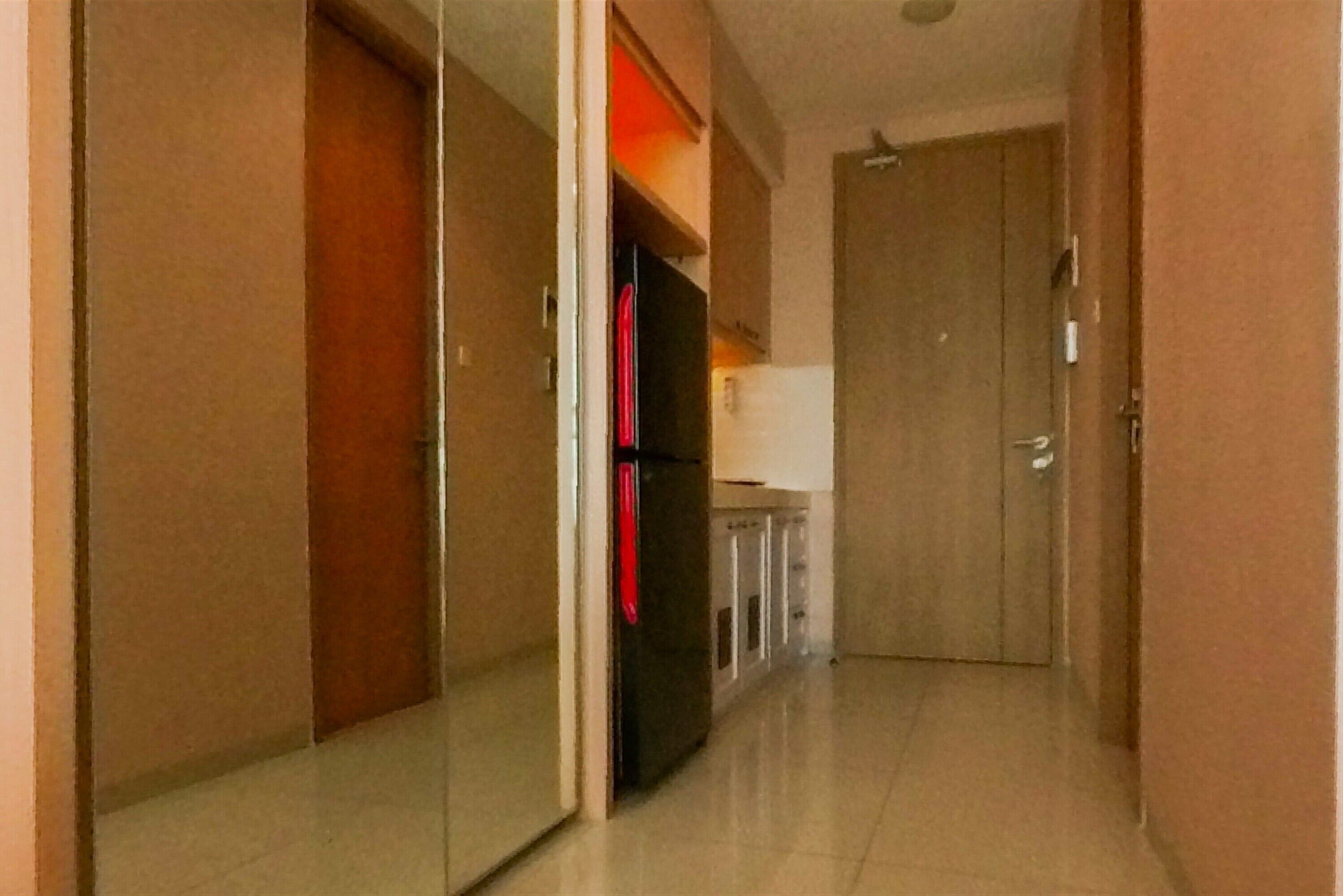 A narrow hallway with a refrigerator, cabinets, and a door at the end.