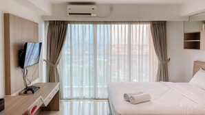 Habitación de hotel con cama, escritorio con computadora, televisor y ventana con cortinas.