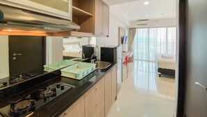 Una cocina moderna con estufa, lavamanos y armarios, que da paso a un dormitorio con cama y cortinas.