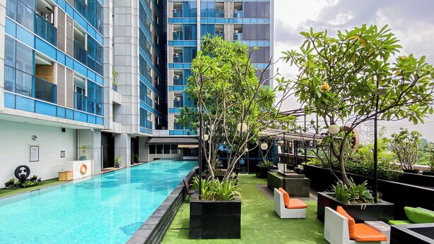 Área de piscina en la azotea con piscina azul cristalina, rodeada de césped artificial verde y plantas en macetas.