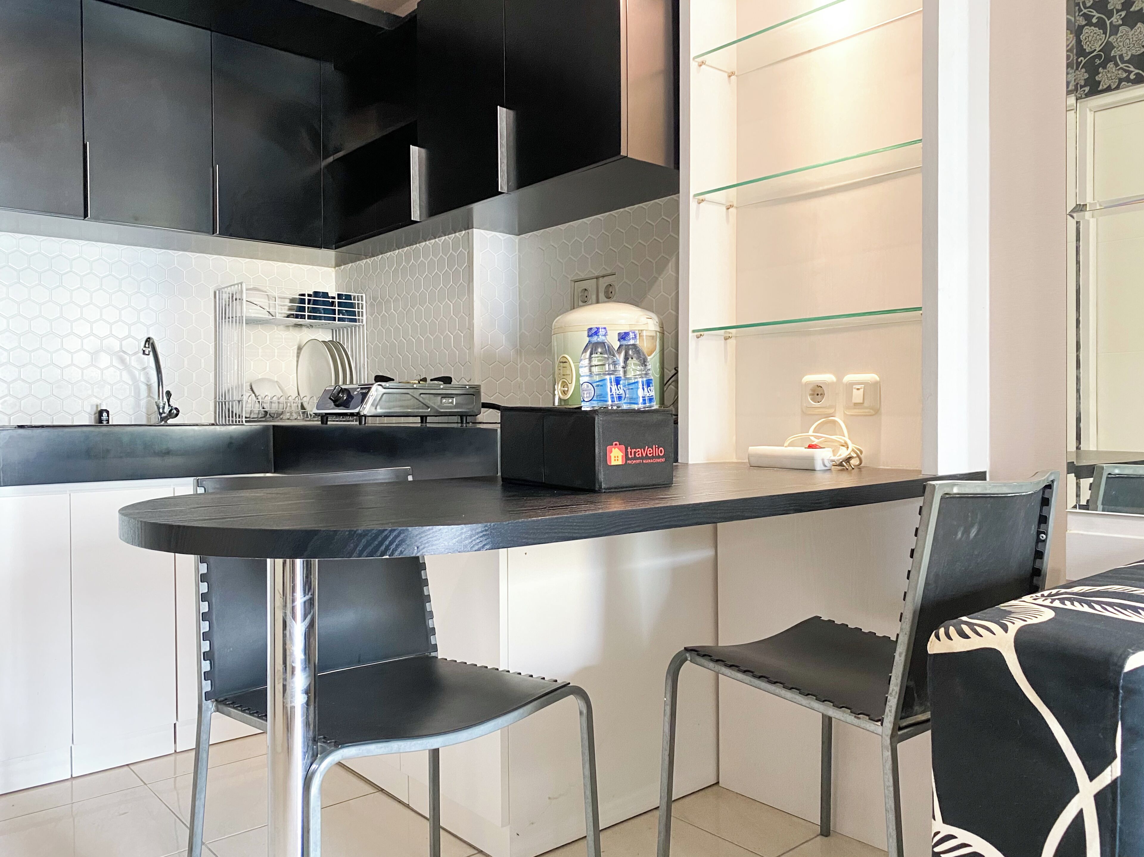 A modern kitchen with a black countertop, two bar stools, and a water dispenser.