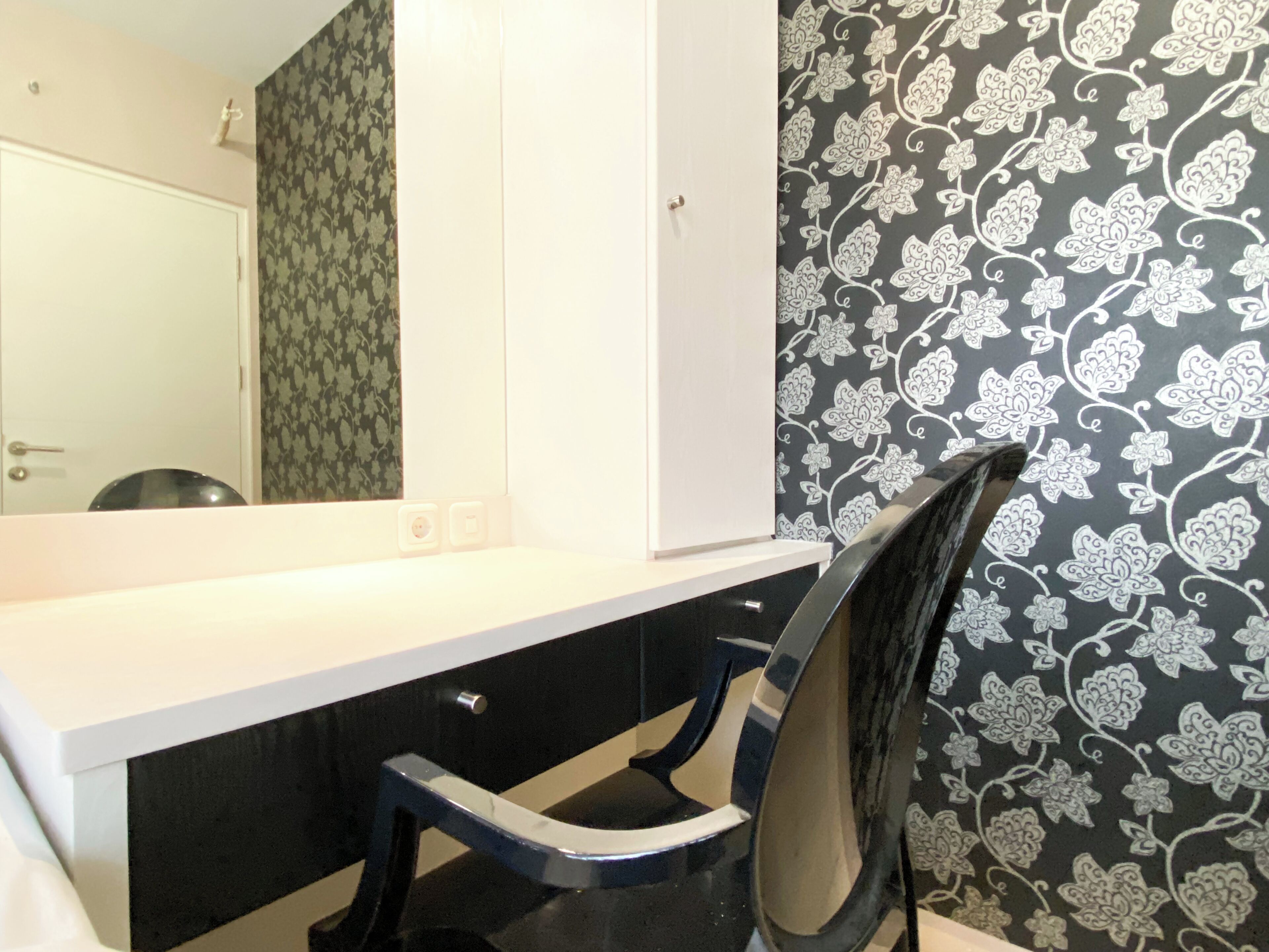 A bathroom with a white vanity, black chair, and floral wallpaper.
