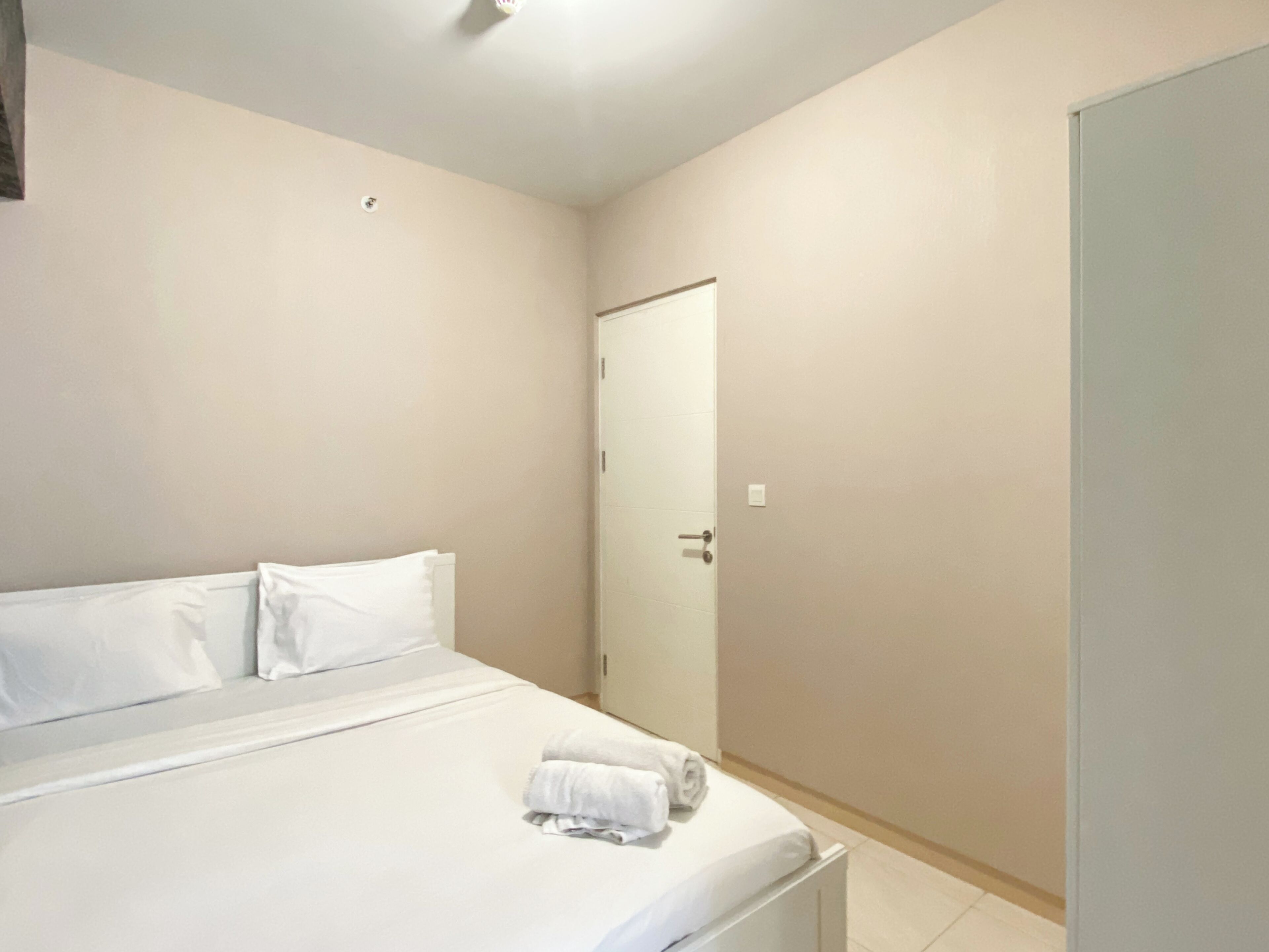 A bedroom with a bed, pillows, a rolled towel, and a door.