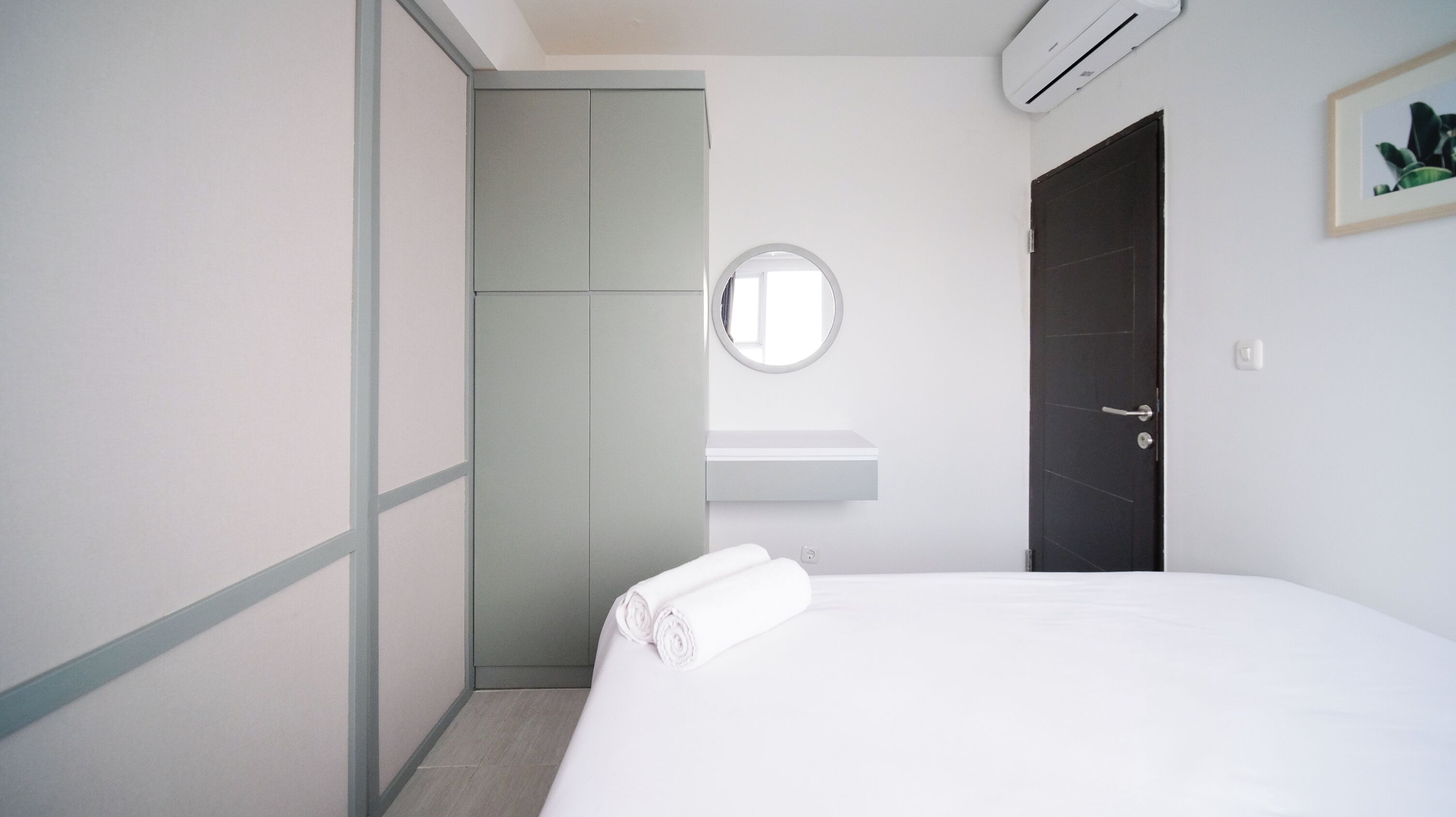 Ein schlicht eingerichtetes Hotelzimmer mit einem Bett, einem runden Spiegel, einem weißen Waschbecken und einer dunklen Tür.
