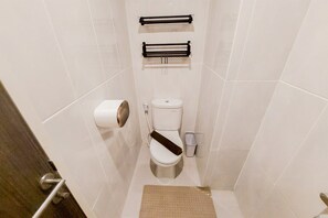 A small, narrow bathroom with a toilet, two towel racks, a trash bin, and a toilet paper holder. - Restful And Comfortable Studio Serpong Garden Apartment (Cisauk)