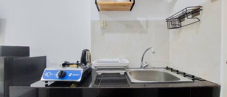 Una cocina compacta con estufa a gas, un lavamanos y una encimera. Hay escurreplatos y un pequeño estante sobre el lavamanos.