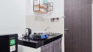 A compact kitchenette with a black countertop, a coffee maker, and a compact stove. - Restful And Comfortable Studio Serpong Garden Apartment (Cisauk)