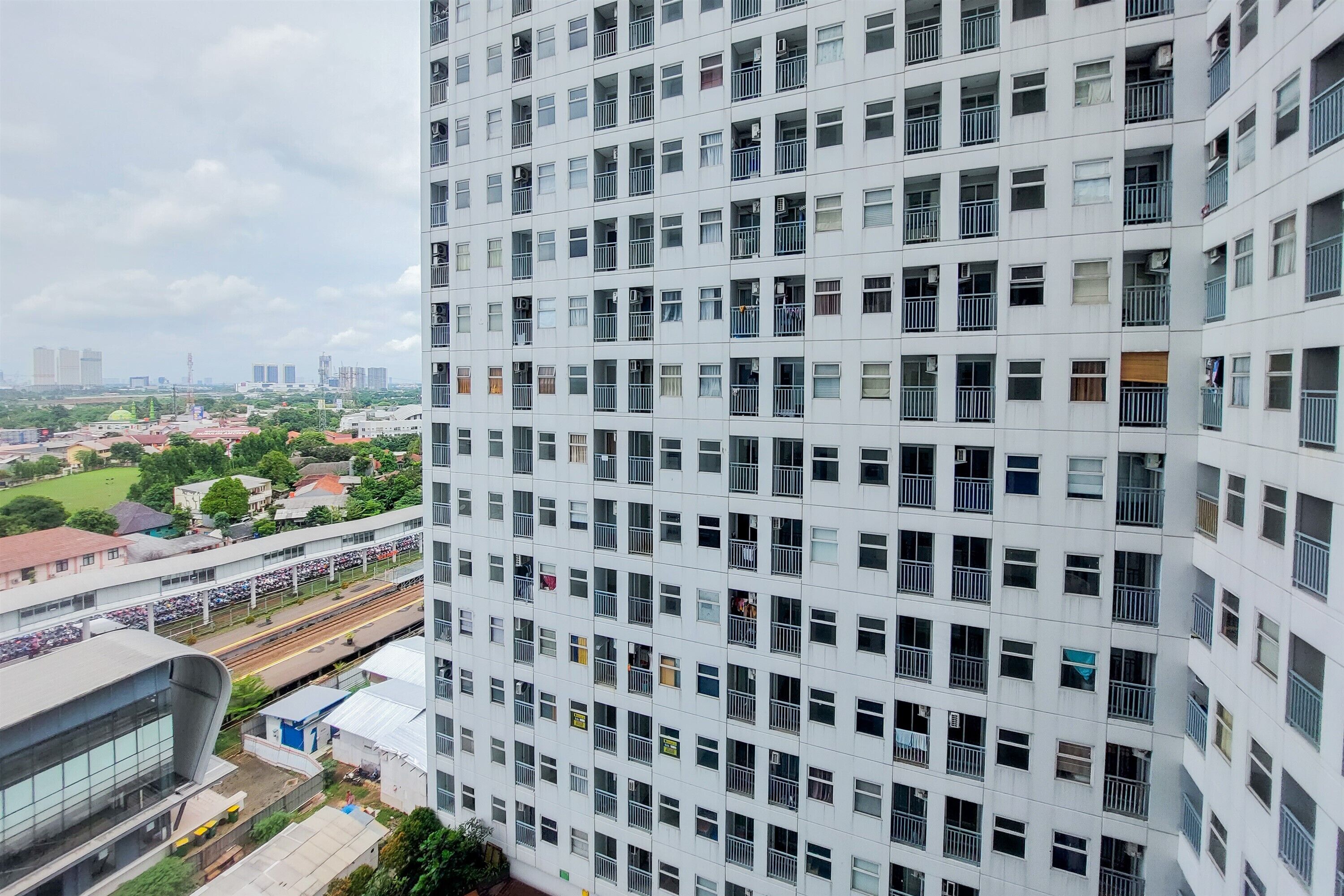 Un immeuble de grande hauteur doté de nombreux balcons et offrant une vue sur une voie ferrée et sur la verdure en contrebas.