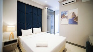 A modern hotel room with a large bed, a bedside table with a lamp, a wardrobe, and artwork on the wall.