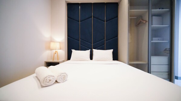 A neatly made bed with white linens, a bedside lamp, and a dark headboard.