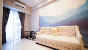 A hotel room with a cream-colored sofa, a small round table, and a large wall mural of mountains.