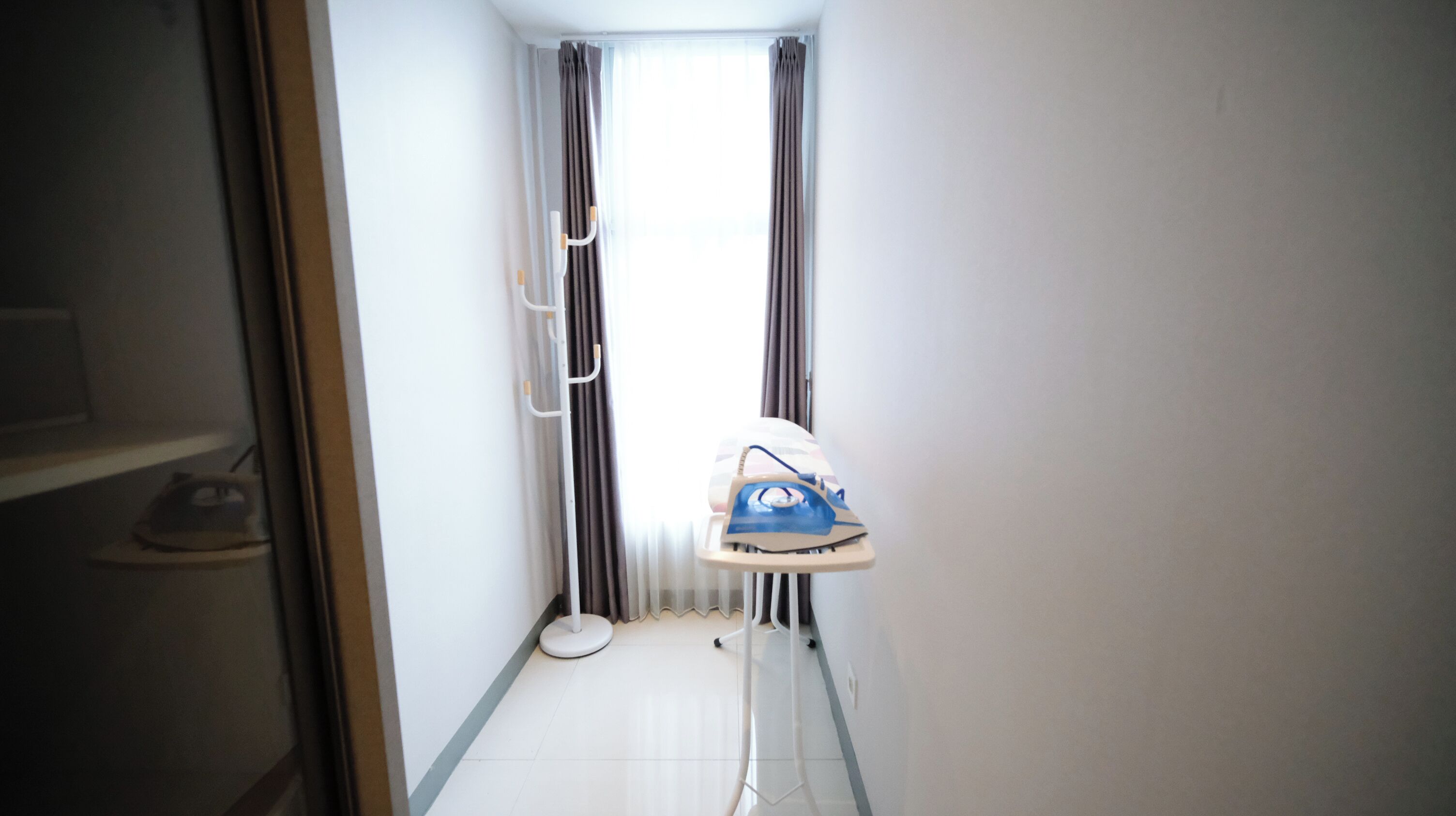 A narrow hallway with a white radiator, a blue ironing board, and a pair of curtains.