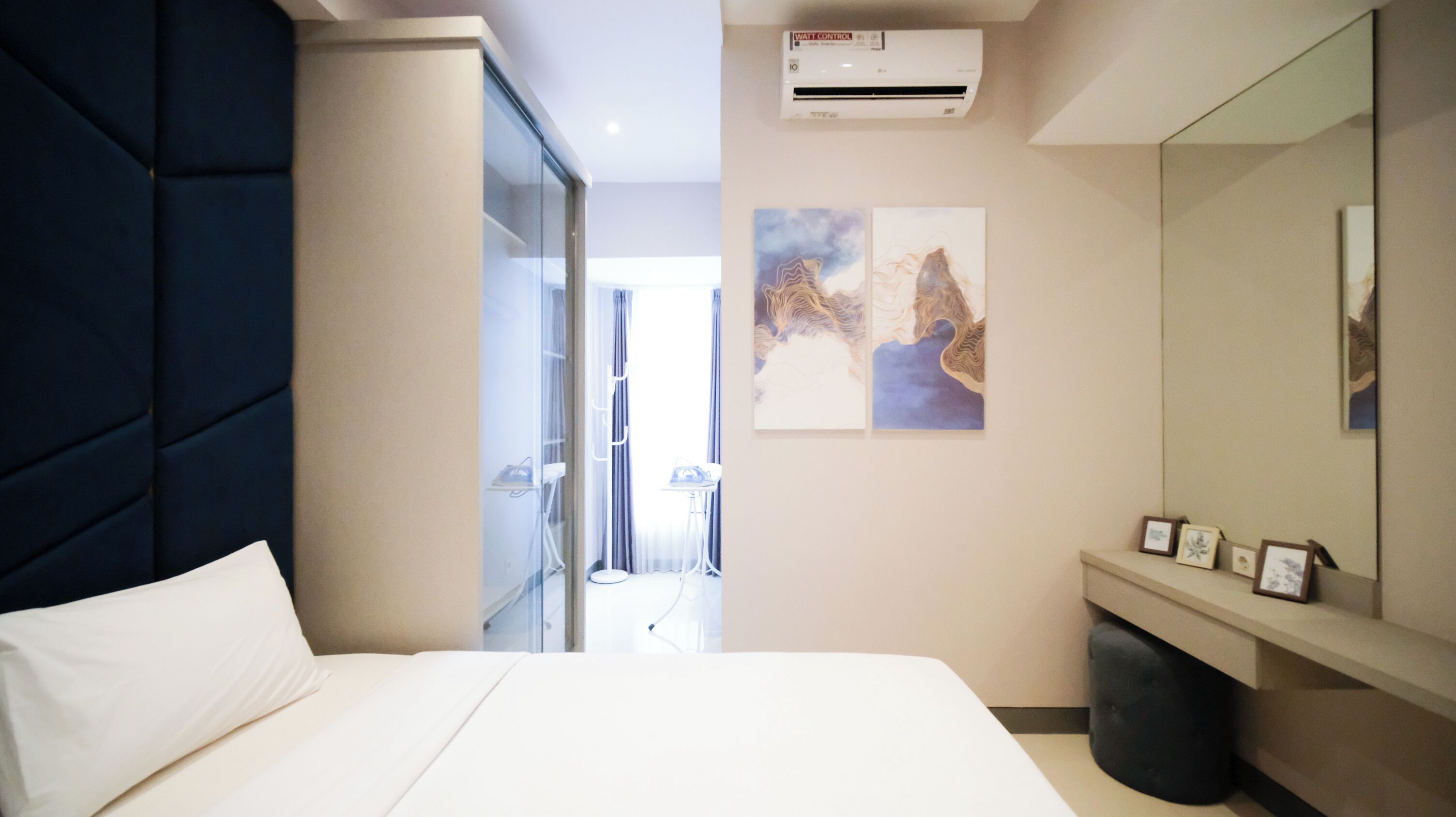 Ein modernes Hotelzimmer mit einem großen Bett, einer Glaseinteilung, einer Wandklimaanlage und einem gerahmten Kunstwerk.