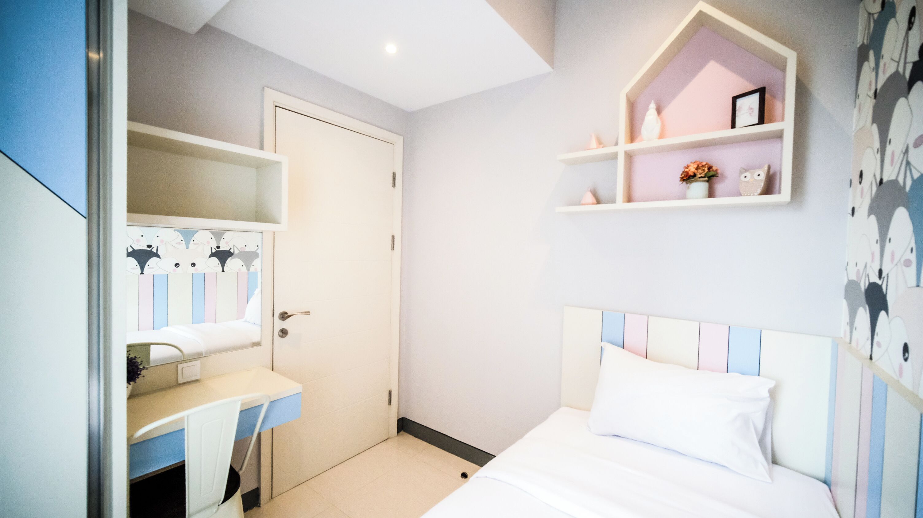 Un dormitorio con cama, escritorio y espejo. En la pared, hay una estantería con objetos decorativos.