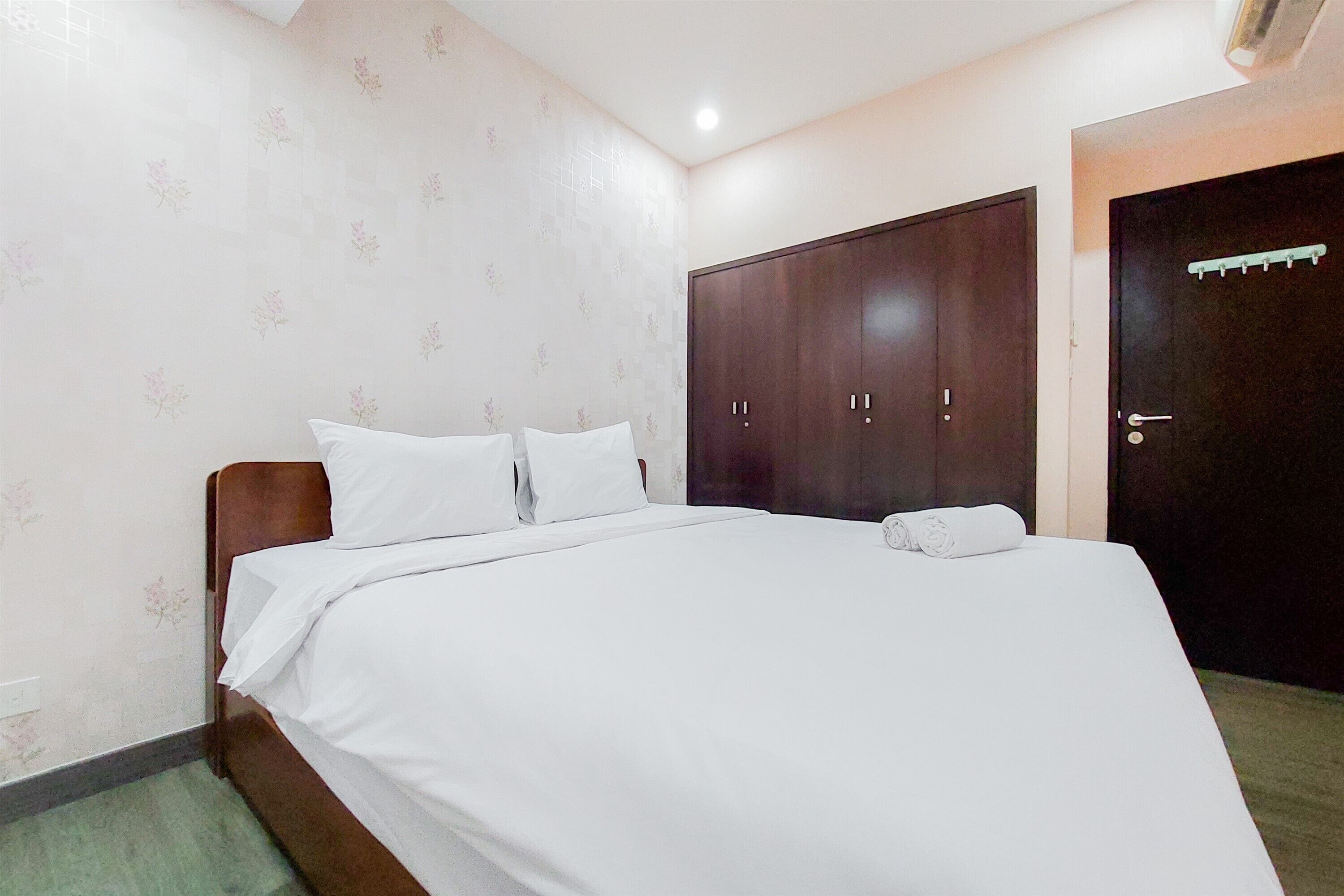 A neatly made bed with white linens in a room with floral wallpaper and a dark wooden wardrobe.