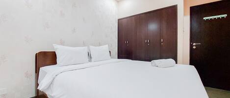 A neatly made bed with white linens in a room with floral wallpaper and a dark wooden wardrobe.