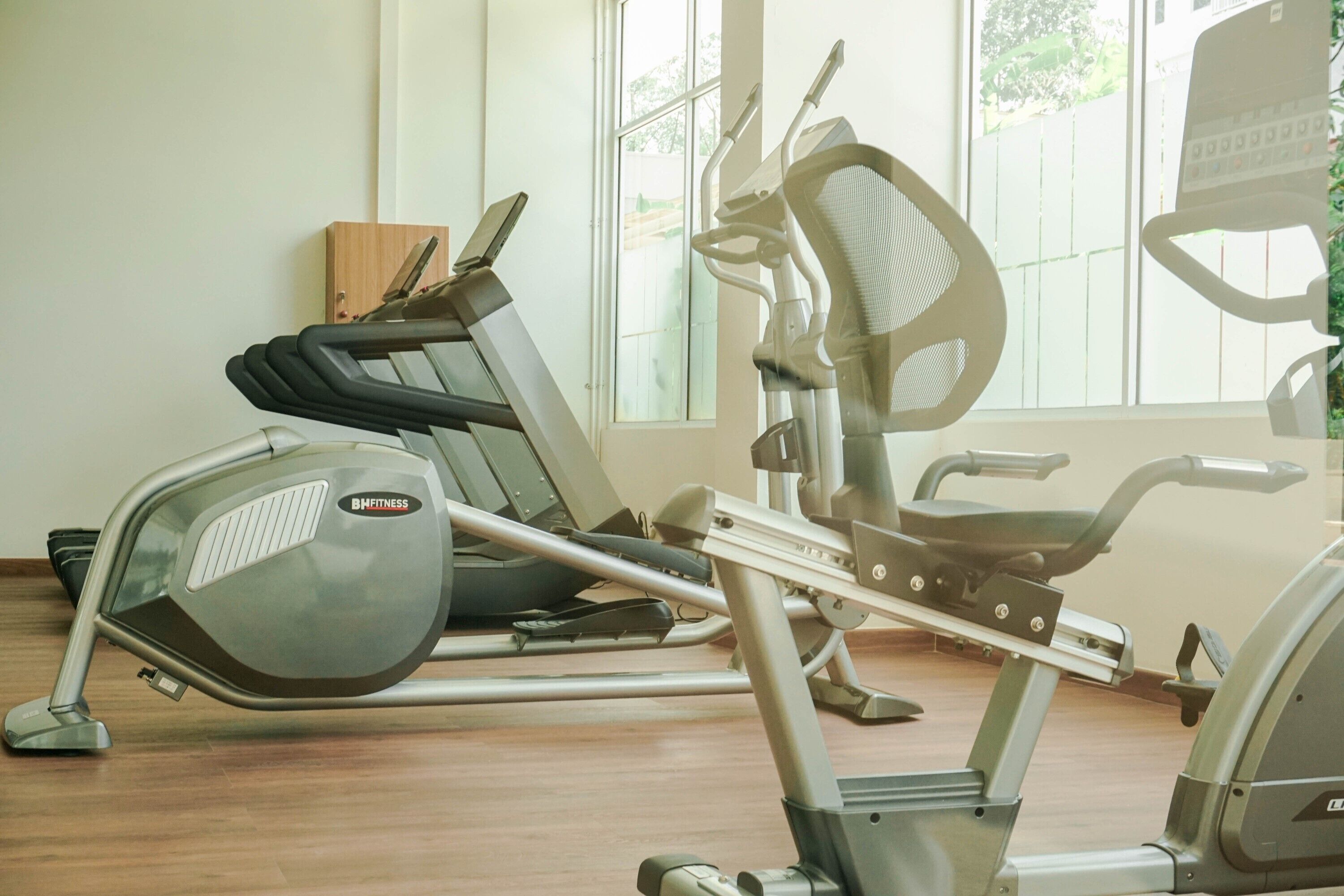 Een sportschool met trainingsapparatuur, waaronder een loopband en een elliptische machine, in een ruimte met grote ramen.