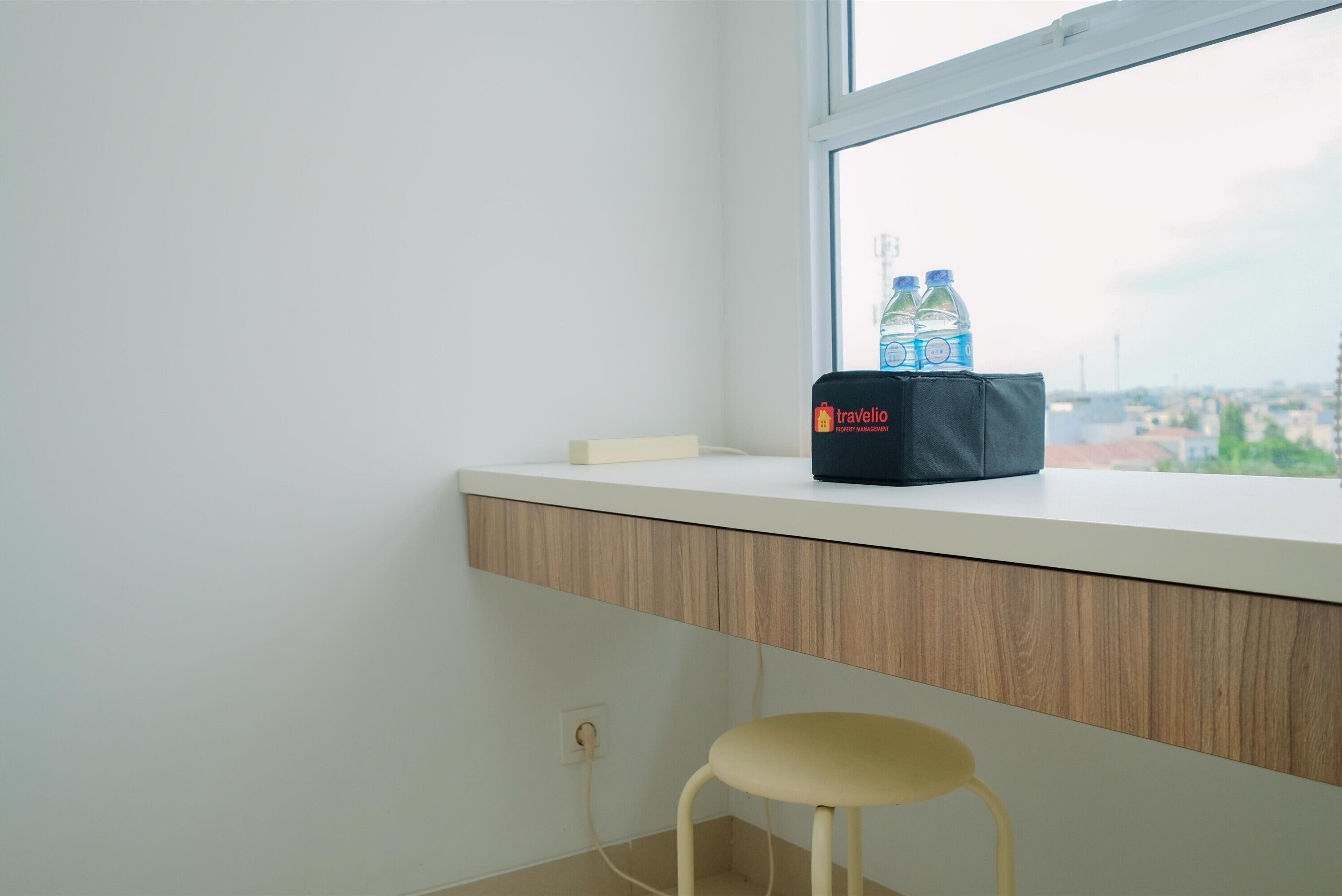 A window seat with a black bag labeled "Travelio" and two water bottles on a white ledge.