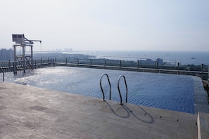 A rooftop pool with a view of the sea and distant buildings. - Comfy And Modern Look 2Br Northland Ancol Apartment (Jakarta)