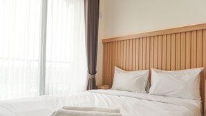 A hotel room with a large bed, wooden headboard, and a view of the city through sheer curtains. - Cozy And Well Furnished Studio Sky House Bsd Apartment (Pagedangan)