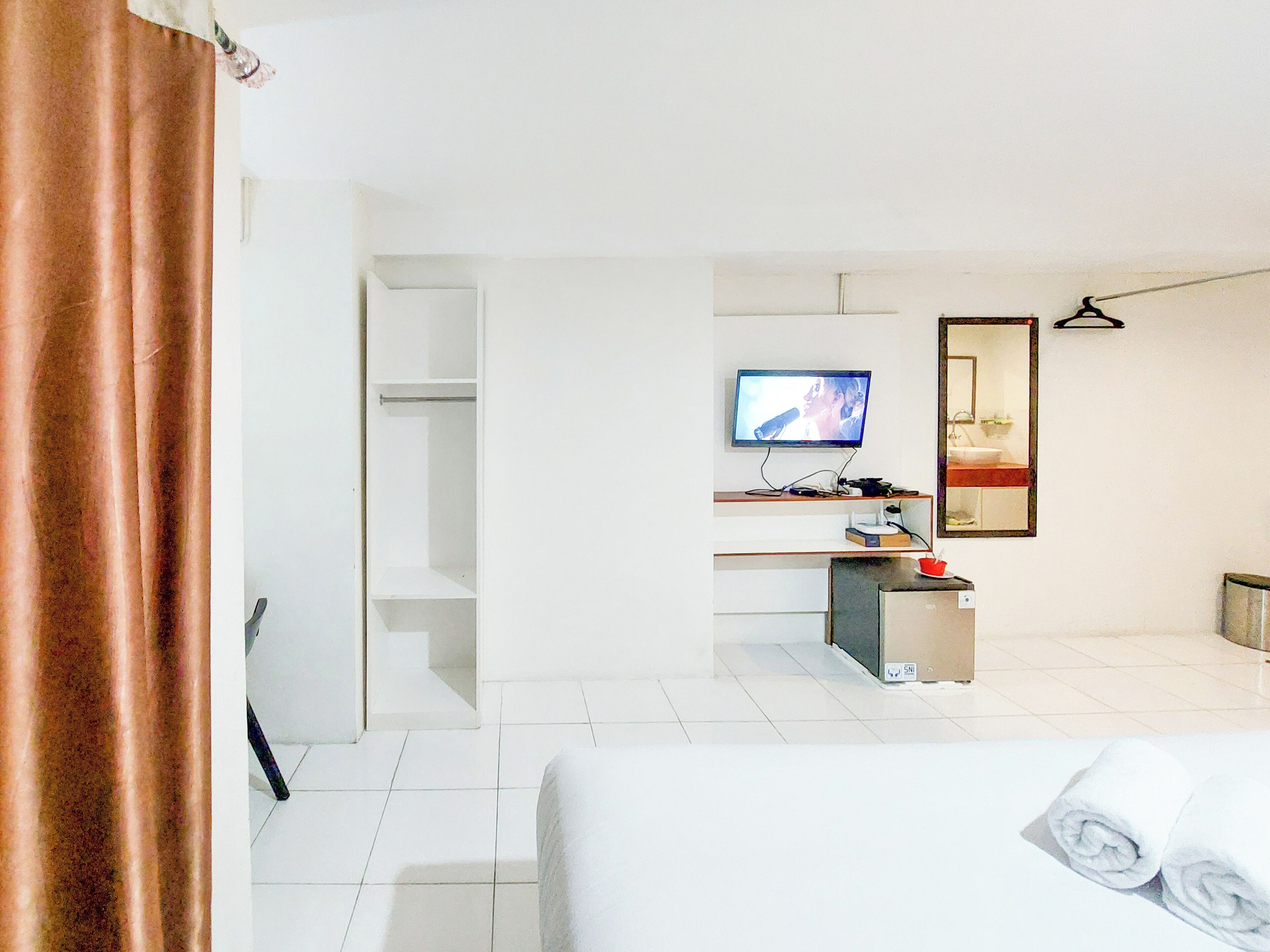 A hotel room with a bed, a TV, a desk with a computer, a mirror, and a bathroom with a sink and toilet.