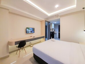 A modern hotel room with a large bed, a TV mounted on the wall, a desk with a chair, and a bathroom visible through an open door.