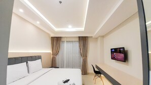 Una habitación de hotel moderna con una cama bien hecha, un escritorio con silla, un televisor y un gran ventanal con cortinas.