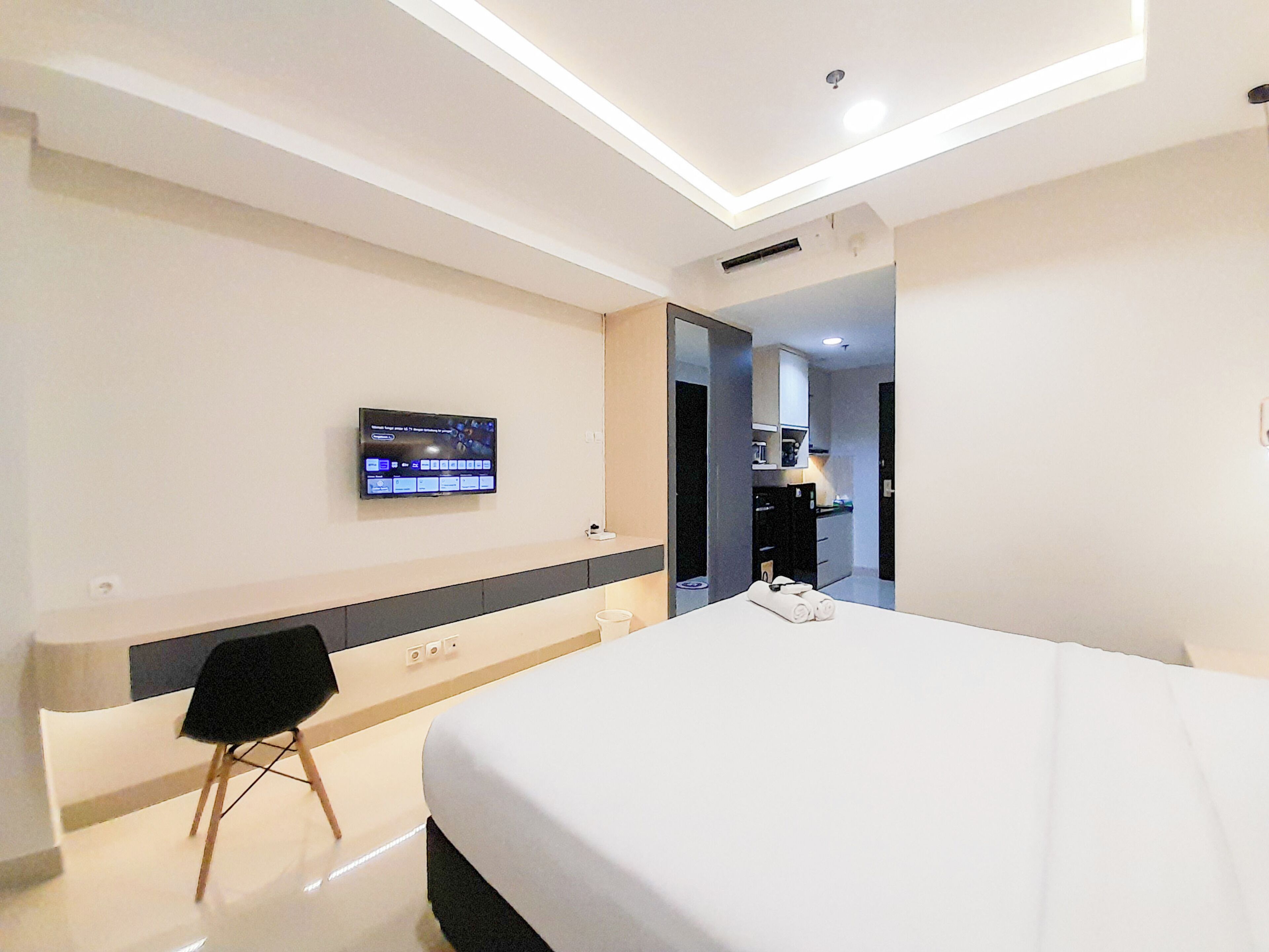Une chambre d’hôtel moderne avec un grand lit, un téléviseur à écran plat fixé au mur, un petit coin salon et une kitchenette à l’arrière-plan.