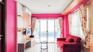 Een woonkamer met een rode bank, een klein rond tafeltje en een televisie op een dressoir.