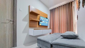 Ett modernt rum med en grå soffa, en väggmonterad TV och en hylla i trä.