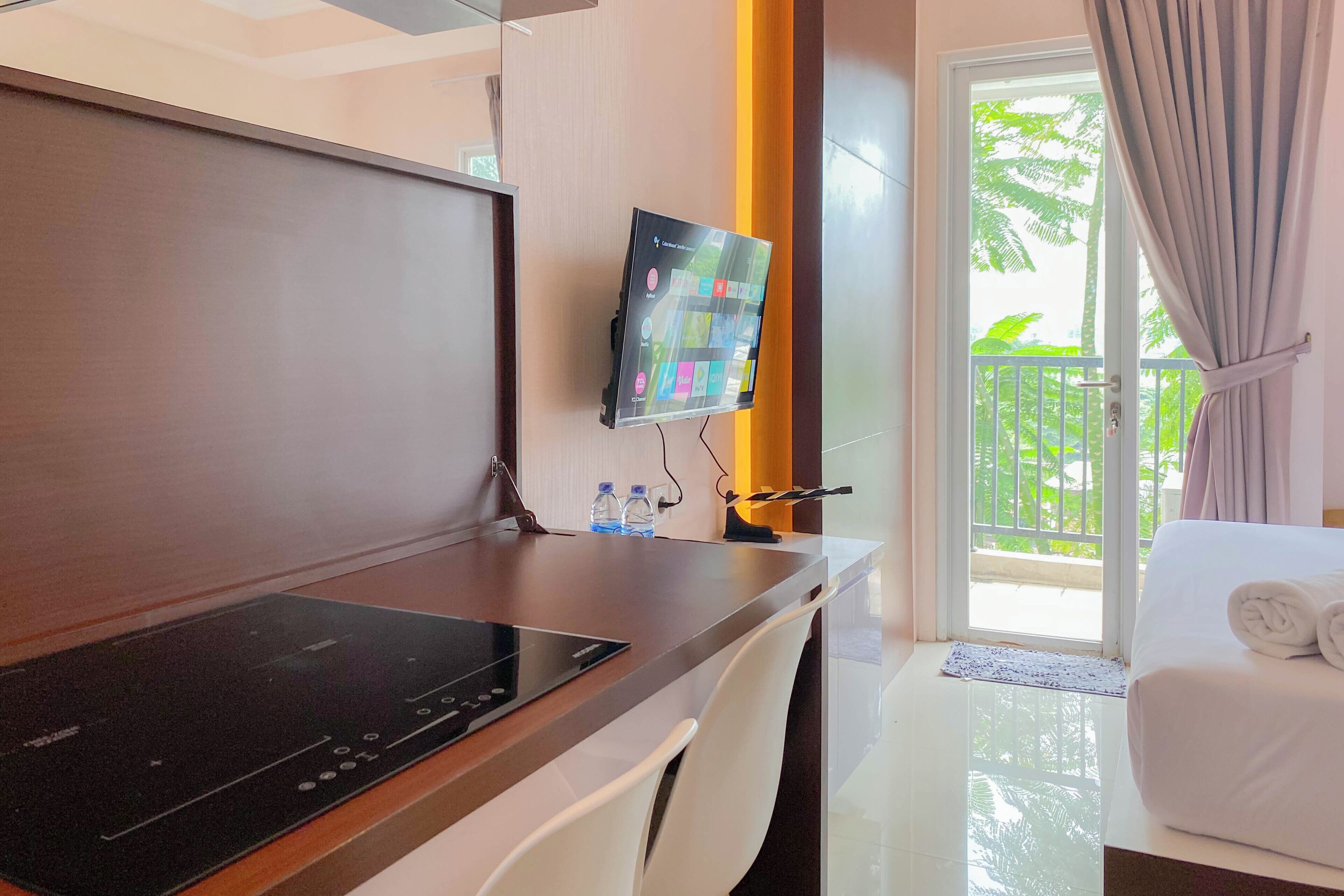 Habitación de hotel con escritorio, televisión de pantalla plana, cama con toallas dobladas y balcón con vista a follaje.