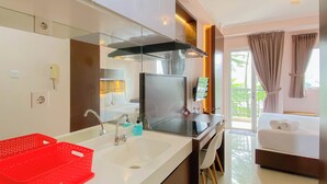 A modern hotel room with a large bed, a TV, a sink with red baskets, and a balcony with curtains. - Well Design And Homey Studio Signature Park Grande Apartment (Jakarta)