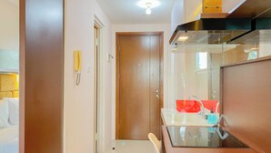 A modern bathroom with a glass shower enclosure, a wooden door, and a white sink with a red soap dispenser. - Well Design And Homey Studio Signature Park Grande Apartment (Jakarta)