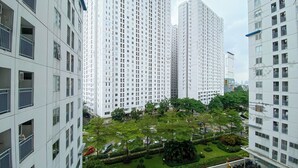 A high-rise residential building with multiple floors, balconies, and a well-maintained green space with trees and shrubs. - Cozy 2Br With Modern Design Bassura City Apartment Near Mall (Jakarta)