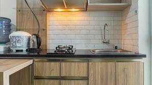 A modern kitchen with wooden cabinets, a gas stove, a sink, and a stainless steel faucet. - Cozy 2Br With Modern Design Bassura City Apartment Near Mall (Jakarta)
