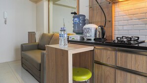 A compact kitchen with a sofa, a water dispenser, a kettle, and a stove. - Cozy 2Br With Modern Design Bassura City Apartment Near Mall (Jakarta)