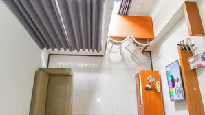 A room with a sofa, a wooden table, a TV, and a desk with a phone and a remote control. - Good Deal Studio Loft At Nifarro Park Apartment (Jakarta)