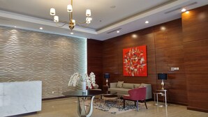 A modern living room with a marble fireplace, a chandelier, a sofa, a red armchair, and a large abstract painting on the wall. - Good Deal Studio Loft At Nifarro Park Apartment (Jakarta)