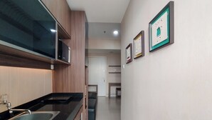 Cozinha moderna com bancada preta, pia de aço inoxidável e armários de madeira. Há quadros nas paredes e uma porta que dá para outro cômodo.