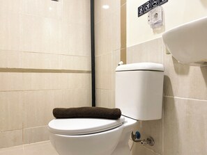 Moderni kylpyhuone, jossa on wc, pyyhe ja seinälle kiinnitetty wc-paperiteline.