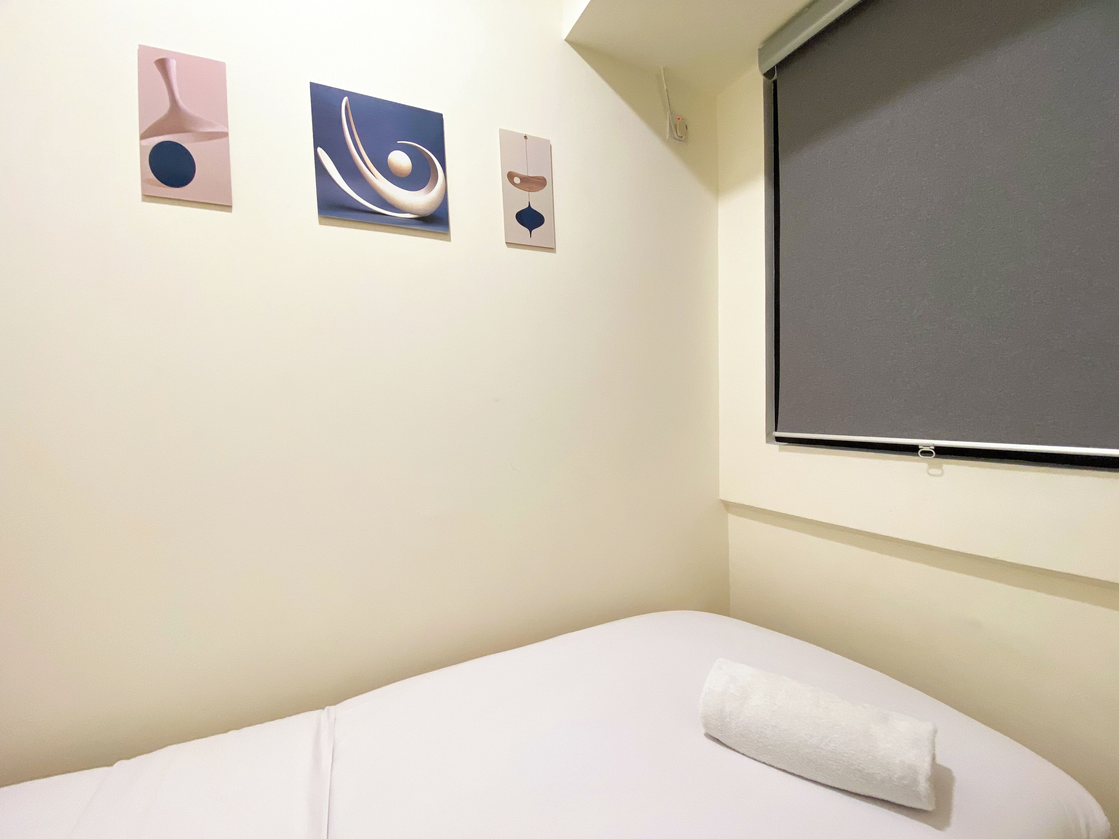 Ein Hotelzimmer mit einem Einzelbett, einem Fenster mit Jalousie und drei abstrakten Wandbildern.