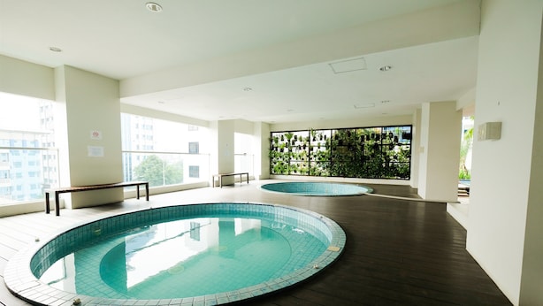 A modern indoor swimming pool with a wooden deck, large windows, and a wall of hanging plants. - Good Choice And Elegant 2Br Apartment Capitol Park Residence (Jakarta)