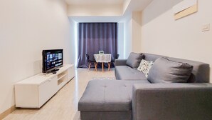 Una sala de estar moderna con un sofá gris, un mueble de TV blanco y una mesita con mantel.