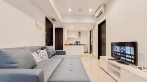 Una sala moderna con un sofá gris, un televisor de pantalla plana y una cocina al fondo.